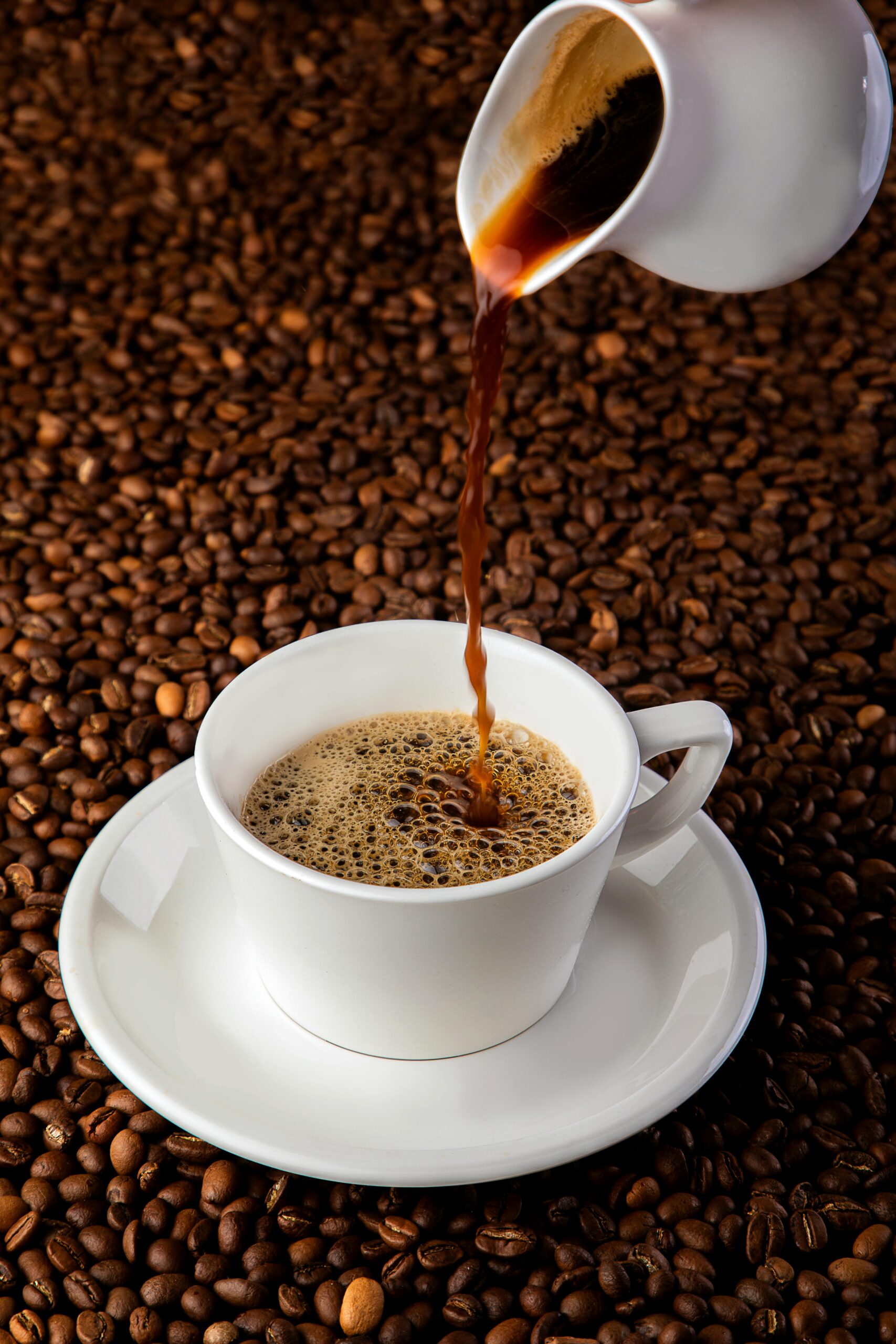 Close-up of hot coffee being poured into a white cup with coffee beans background.