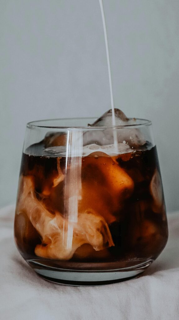 Close-up of refreshing iced coffee in a glass with a swirl of milk, creating a perfect cool beverage.